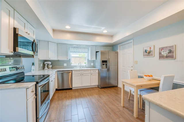 kitchen with light wood-style flooring, stainless steel appliances, a sink, light countertops, and decorative backsplash