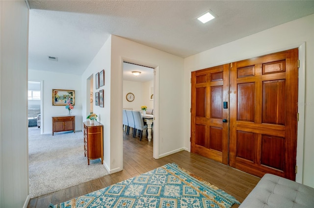 hallway featuring visible vents, a textured ceiling, baseboards, and wood finished floors