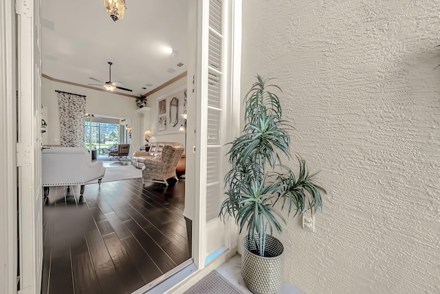 hall with a textured wall, ornamental molding, and wood finished floors