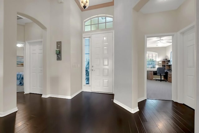 foyer with arched walkways, dark wood-style flooring, and baseboards