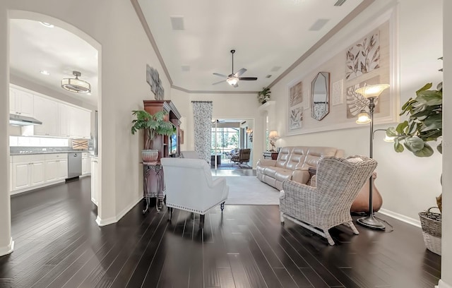 living room with arched walkways, dark wood-style flooring, crown molding, a ceiling fan, and baseboards