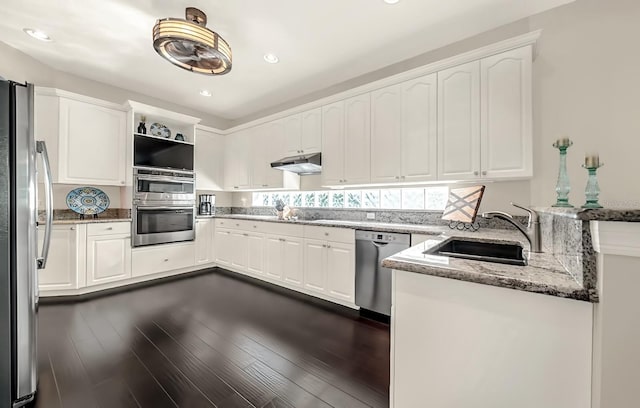 kitchen with light stone counters, dark wood finished floors, appliances with stainless steel finishes, a sink, and under cabinet range hood