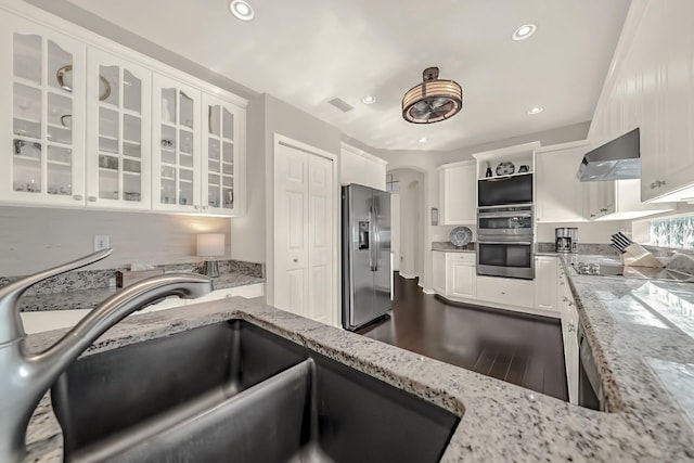 kitchen with stainless steel appliances, a sink, white cabinets, light stone countertops, and wall chimney exhaust hood