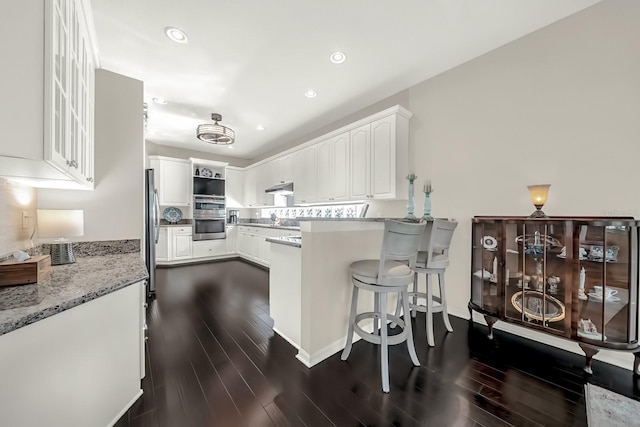 kitchen featuring dark wood-style floors, stainless steel appliances, white cabinets, a peninsula, and under cabinet range hood