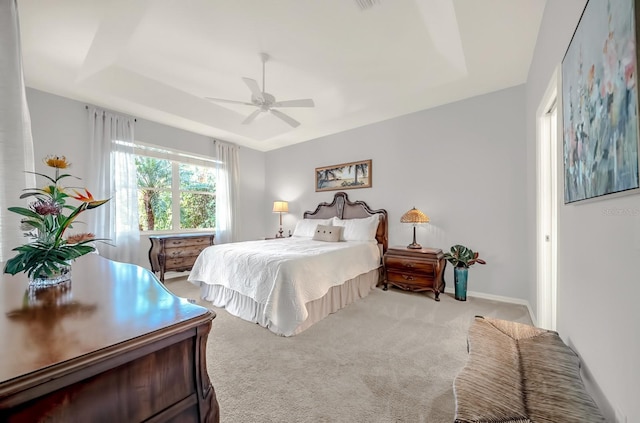 carpeted bedroom featuring a tray ceiling, a ceiling fan, and baseboards