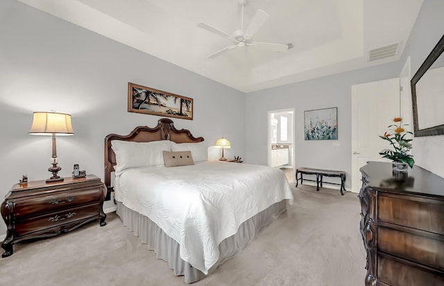 bedroom with ceiling fan, light carpet, visible vents, a tray ceiling, and ensuite bath