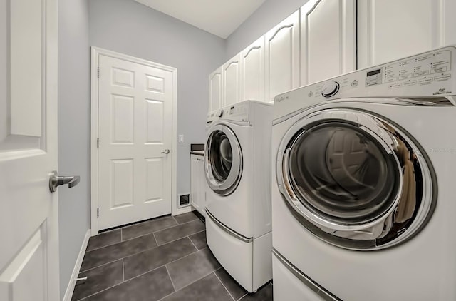 clothes washing area with cabinet space, dark tile patterned floors, baseboards, and separate washer and dryer