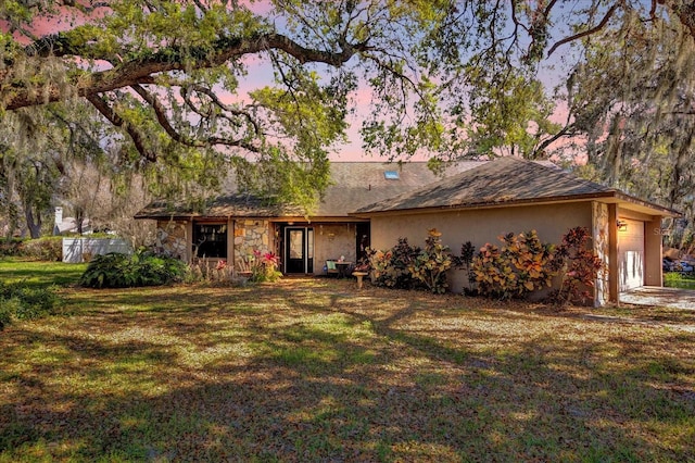 view of front of home featuring a front yard, stone siding, an attached garage, and stucco siding