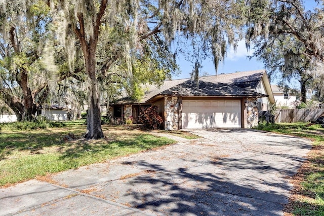 view of front of property featuring a garage, stone siding, fence, and driveway