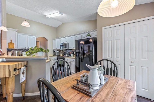 dining area featuring arched walkways, vaulted ceiling, and a textured ceiling