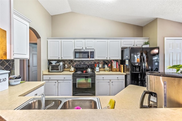 kitchen featuring lofted ceiling, a sink, white cabinetry, backsplash, and black appliances