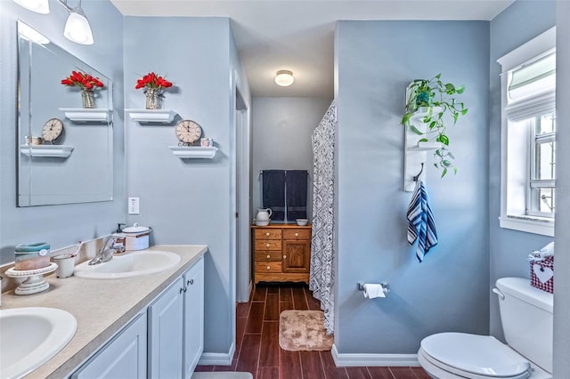 bathroom featuring double vanity, wood finish floors, a sink, and toilet