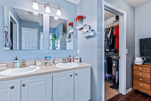 full bathroom featuring double vanity, a walk in closet, a sink, and wood finish floors