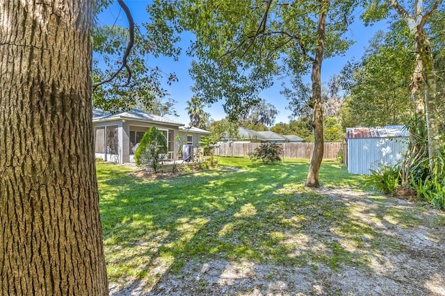 view of yard with an outbuilding, a sunroom, fence, and a storage shed