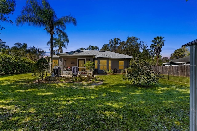 back of house at dusk featuring a yard, fence, and stucco siding