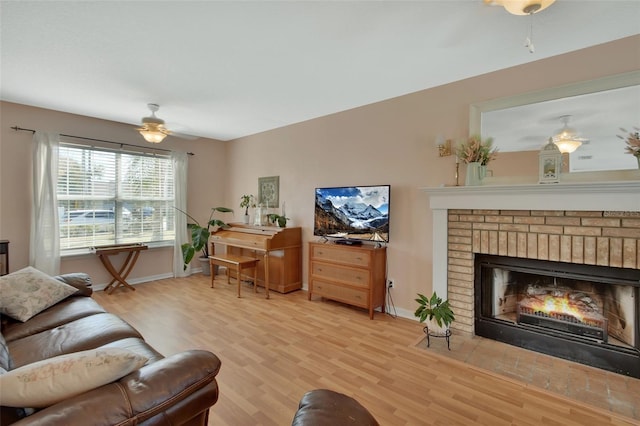 living room featuring light wood-type flooring, a brick fireplace, ceiling fan, and baseboards