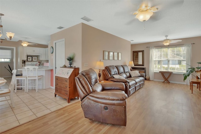 living room with a ceiling fan, light wood-type flooring, visible vents, and a textured ceiling