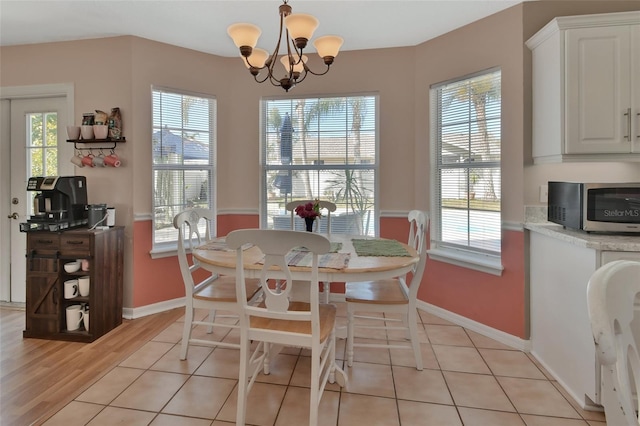 dining space with light wood-type flooring, plenty of natural light, baseboards, and a notable chandelier