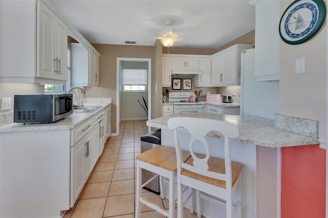 kitchen with white electric range oven, stainless steel microwave, light tile patterned flooring, white cabinets, and a sink