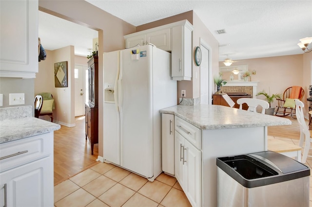 kitchen featuring a brick fireplace, visible vents, white refrigerator with ice dispenser, and white cabinetry