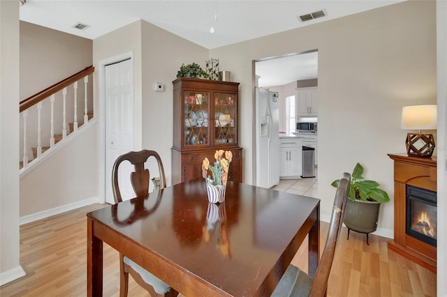 dining area with light wood finished floors, stairway, a glass covered fireplace, and visible vents