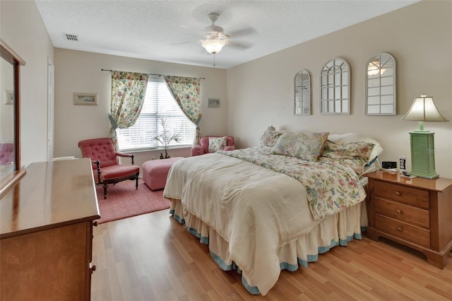 bedroom with light wood-style floors, ceiling fan, visible vents, and a textured ceiling