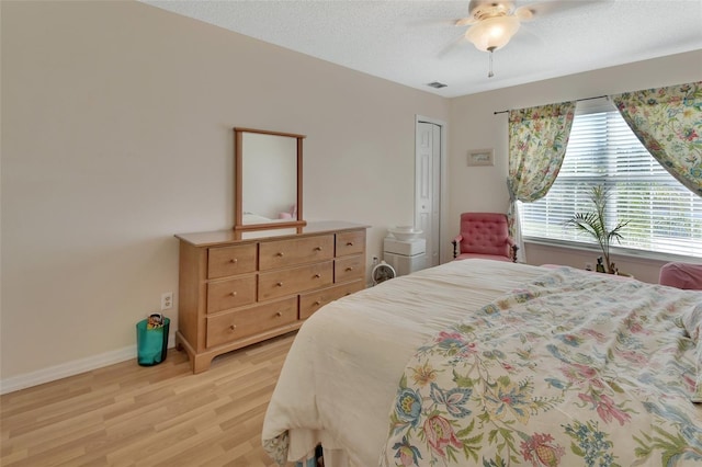 bedroom with a textured ceiling, light wood-style flooring, visible vents, a ceiling fan, and baseboards