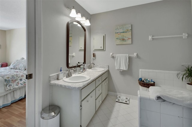 ensuite bathroom with double vanity, ensuite bath, baseboards, and a sink