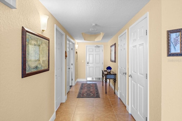 corridor with light tile patterned floors, a textured ceiling, and baseboards