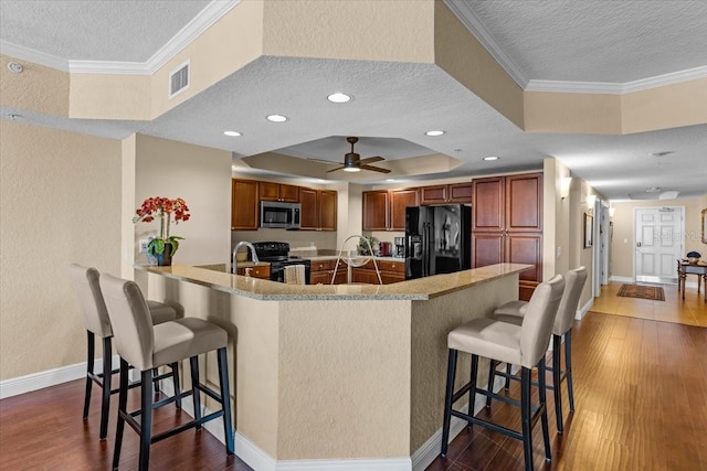 kitchen featuring visible vents, dark wood-style floors, black appliances, a tray ceiling, and a kitchen bar