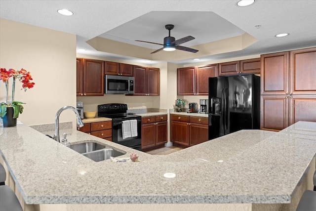 kitchen with ceiling fan, a peninsula, a sink, black appliances, and a tray ceiling