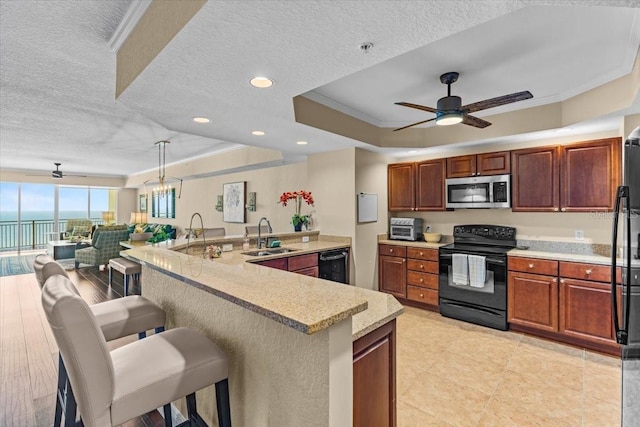 kitchen with a tray ceiling, light countertops, ornamental molding, a sink, and black appliances