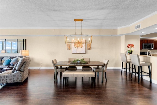 dining space with a textured ceiling, dark wood-style flooring, visible vents, baseboards, and crown molding