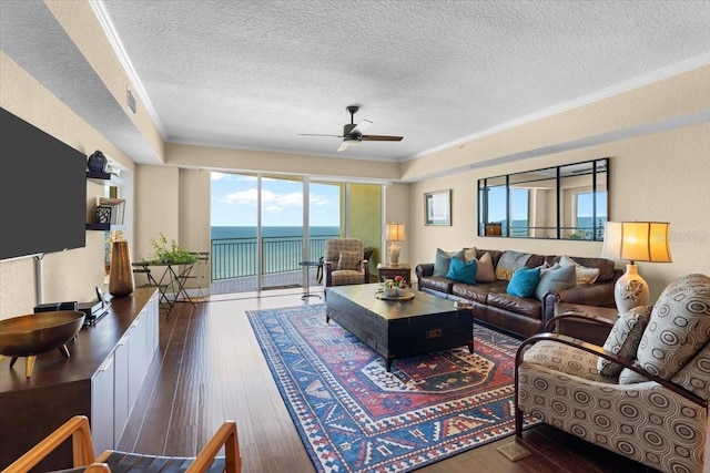 living area with a water view, a textured ceiling, dark wood finished floors, and crown molding