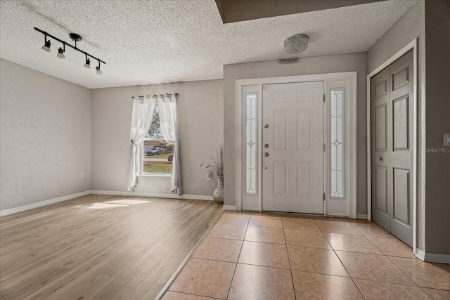 entrance foyer featuring track lighting, baseboards, wood finished floors, a textured wall, and a textured ceiling