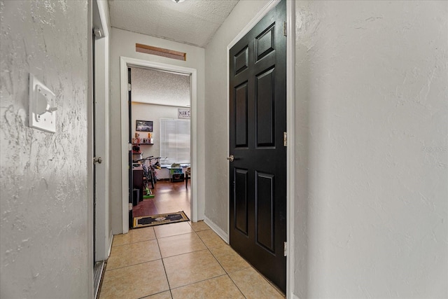 hall featuring light tile patterned floors, a textured wall, and a textured ceiling