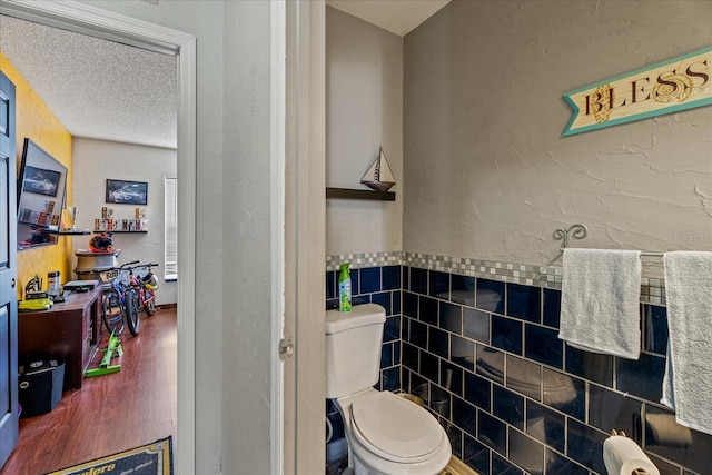 bathroom featuring wood finished floors, a textured ceiling, tile walls, toilet, and a textured wall