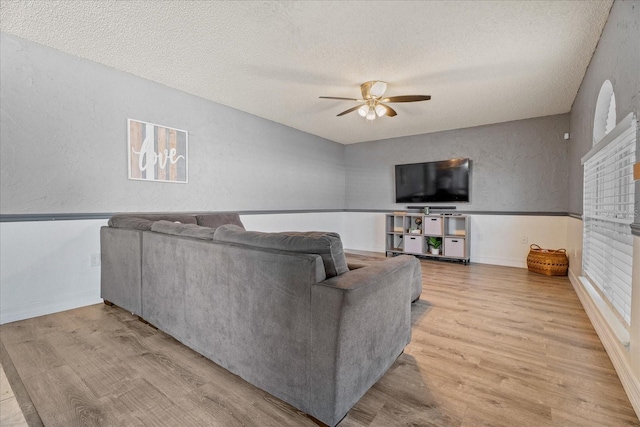 living area featuring ceiling fan, wood finished floors, a textured wall, and a textured ceiling