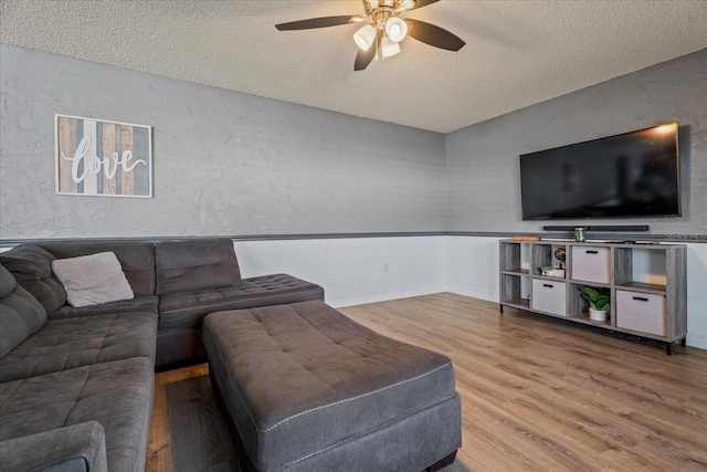 living room with a textured ceiling, a ceiling fan, a textured wall, and wood finished floors