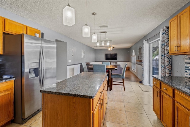 kitchen with a center island, brown cabinetry, light tile patterned floors, hanging light fixtures, and stainless steel fridge