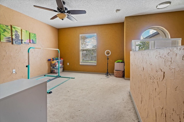 exercise area featuring a ceiling fan, a textured ceiling, carpet flooring, baseboards, and a textured wall