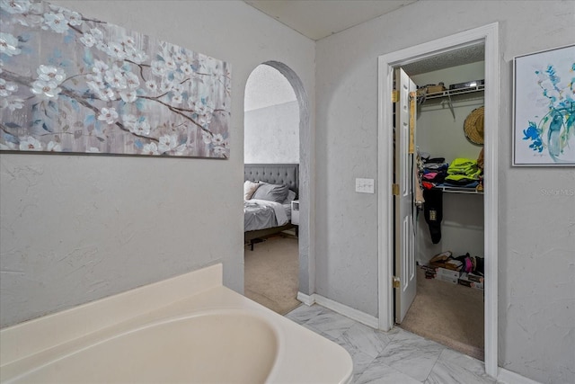 bathroom featuring a walk in closet, a bathing tub, ensuite bathroom, a textured wall, and marble finish floor