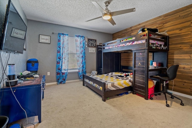 carpeted bedroom with baseboards, a textured ceiling, ceiling fan, and wooden walls