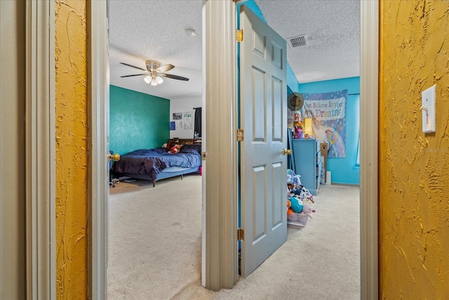 hall with carpet flooring, a textured ceiling, visible vents, and a textured wall