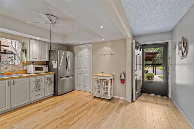 kitchen with a healthy amount of sunlight, white microwave, light wood finished floors, freestanding refrigerator, and a sink