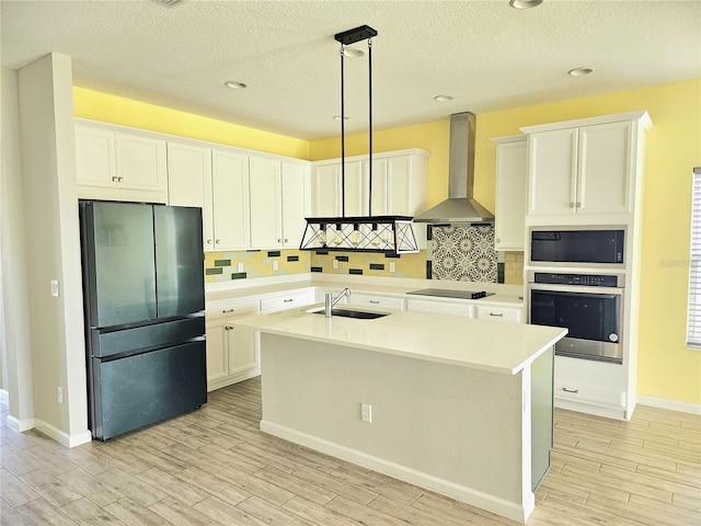 kitchen featuring a sink, stainless steel oven, wall chimney range hood, freestanding refrigerator, and built in microwave