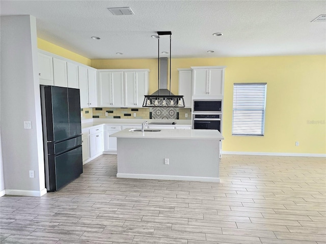 kitchen with stainless steel oven, light countertops, freestanding refrigerator, built in microwave, and wall chimney exhaust hood