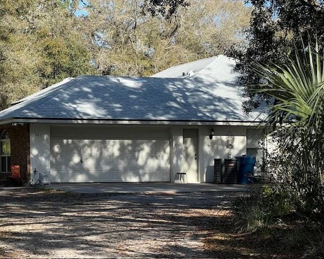 view of side of property featuring a garage, driveway, central AC, and a shingled roof