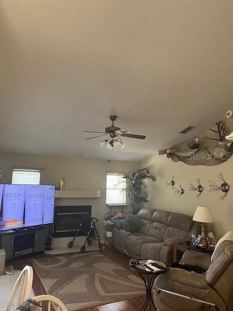 living area with a textured ceiling, ceiling fan, a tile fireplace, and visible vents