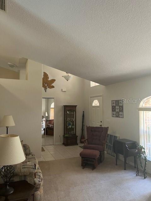 tiled living area with a textured ceiling, visible vents, vaulted ceiling, and carpet flooring